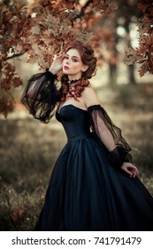 Portrait of magnificent Fashion gothic girl standing in forest .Fantasy art work.Amazing red haired model in black dress looking at camera and posing.Fairytale about young princess 