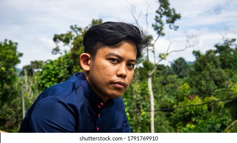 A Portrait Of A Malay Man Model Wearing A Blue Traditional Baju Melayu With Green Nature Background.