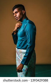 Portrait Of A Malaysian Indian Man In A Striking Blue Traditional Baju Melayu Outfit With A Sampin Wrapped Around His Waist. He Is Dressed Festively To Go Visiting For Raya. He Is Adjusting His Collar