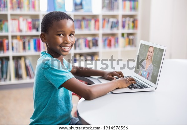 Portrait of male african american student having\
a video call with female teacher on laptop at library. distance\
learning online education\
concept