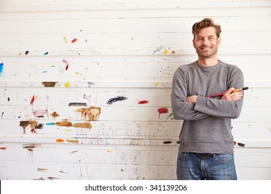 Portrait Of Male Artist Leaning Against Paint Covered Wall - Powered by Shutterstock