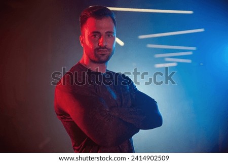 Portrait of a male athlete crossing his arms in a gym, highlighted by blue and red lights with a hazy, backlit setting