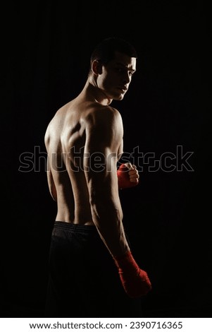 Portrait of male boxer posing in boxing stance, looking over shoulder, against black background.