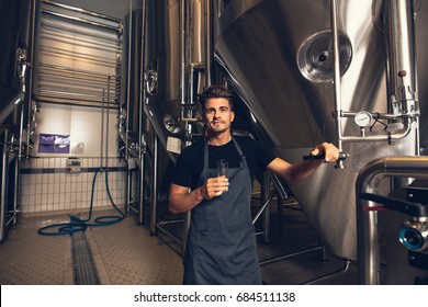 Portrait of male brewer standing by tank in brewery. Man examining the beer in processing section. - Powered by Shutterstock