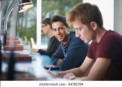 Portrait Of Male College Student Sitting In Library With Laptop Computer, Looking At Camera. Horizontal Shape, Side View, Waist Up