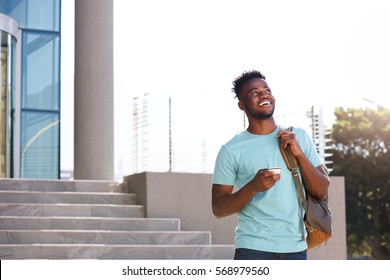 Portrait Of Male College Student Walking By Stairs With Bag And Smart Phone