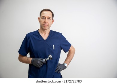 portrait of a male cosmetologist doctor in a blue medical uniform and black gloves with a dermatoscope in his hands. White background