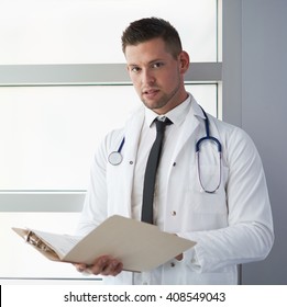 Portrait Of A Male Doctor Holding His Patient Chart In Bright Modern Hospital