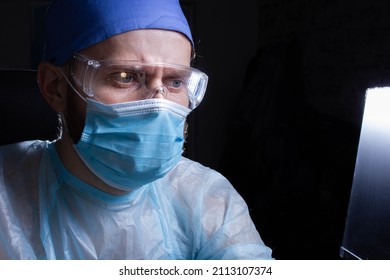 Portrait Of A Male Doctor In A Mask, Glasses And Uniform On A Dark Background. Medic Works In The Office.