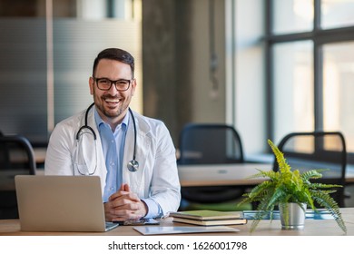 Portrait Of Male Doctor In Office Working At Computer. Serious Doctor Waiting For A Patient. Portrait Of A Smiling Doctor  In His Bright Office.Confident General Practitioner Is Ready To Work