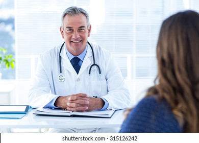 Portrait Of Male Doctor Sitting With Woman At Desk In Hospital