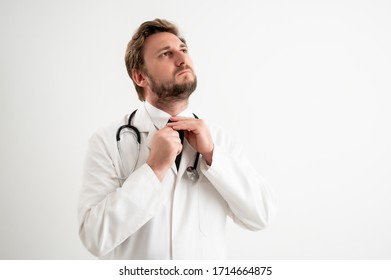 Portrait of male doctor with stethoscope in medical uniform arranges his tie posing on a white isolated background.