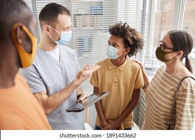 Portrait of male doctor talking to family while standing in waiting room at hospital, all wearing masks