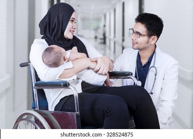 Portrait of male doctor talking with young mother sitting on the wheelchair, shot in the hospital