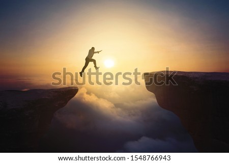 Portrait of male entrepreneur jumping through gap cliff at sunrise time  