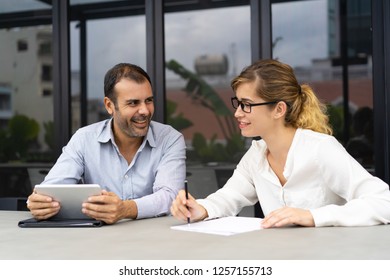 Portrait of male and female colleagues communicating in office. Young Caucasian businesswoman talking to mid adult bearded man with digital tablet. Corporate concept