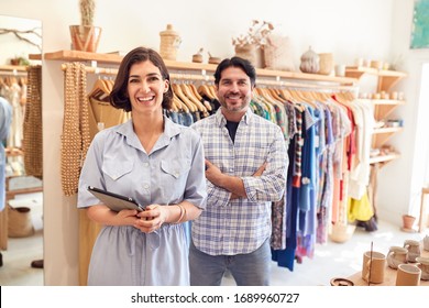 Portrait Of Male And Female Owners Of Fashion Store Checking Stock With Digital Tablet