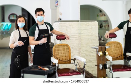 Portrait of male and female skilled hairstylist wearing protective face masks and gloves standing in modern hair studio, ready to work after coronavirus outbreak - Powered by Shutterstock