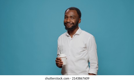 Portrait of male freelancer enjoying cup of coffee in studio, holding mug with latte beverage on work break and timeout. Executive manager smiling and drinking espresso at breakfast.