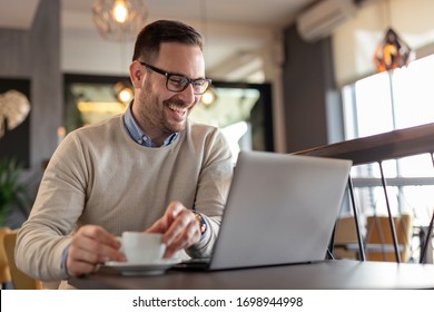 Portrait of a male freelancer sitting at a restaurant table, drinking coffee and working on a laptop computer - Powered by Shutterstock