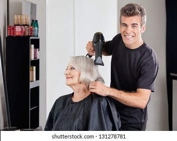 Portrait Of Male Hairdresser With Dryer Setting Up Female Customer's Hair In Parlor