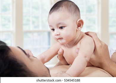 Portrait Of Male Infant Playing With His Dad And Staring At The Father Face, Shot In The Bedroom