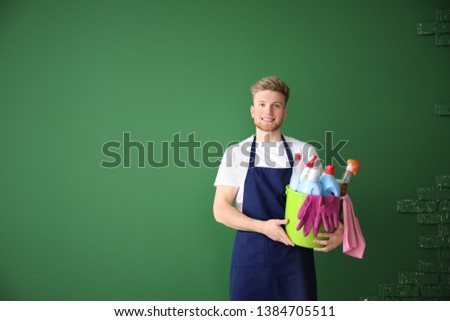 Portrait of male janitor with cleaning supplies on color background