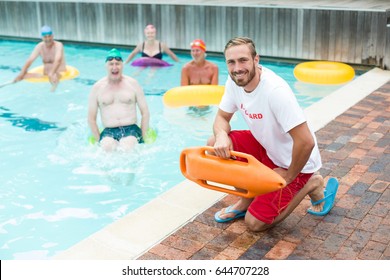 Portrait of male lifeguard crouching while swimmers swimming in pool - Powered by Shutterstock