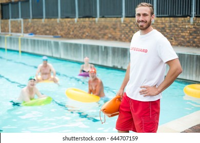 Portrait Of Male Lifeguard Standing While Swimmers Swimming In Pool