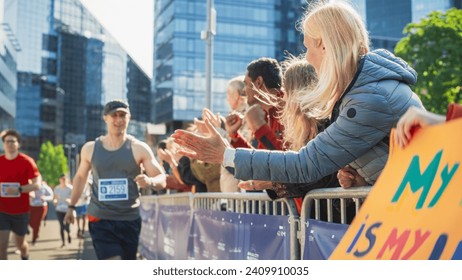 Portrait of a Male Marathon Runner Giving a High Five to Female Family Member in the Audience While Running. Middle Aged Wife Supporting her Husband in a Charity City Marathon Race - Powered by Shutterstock