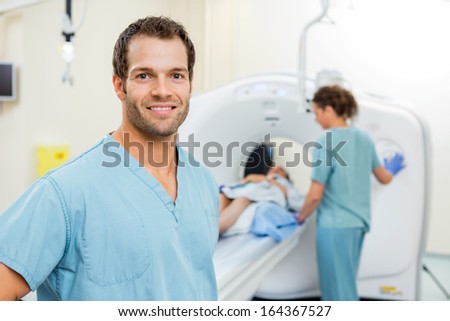Portrait of male nurse with colleague preparing patient for CT scan in examination room