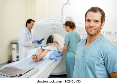 Portrait Of Male Nurse With Colleague And Radiologist Preparing Patient For CT Scan In Examination Room