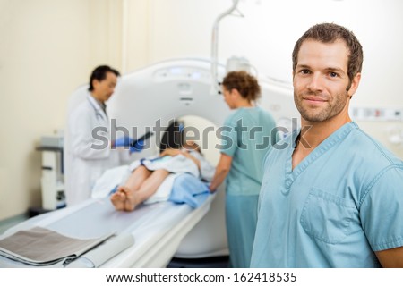 Portrait of male nurse with colleague and radiologist preparing patient for CT scan in examination room