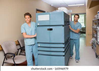 Portrait Of Male Nurse Pushing Trolley While Colleague Assisting Him In Hospital Hallway