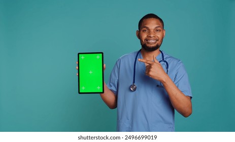 Portrait of male nurse showing medical instructions video on green screen tablet. Hospital employee holding chroma key device, isolated over blue studio background, camera B - Powered by Shutterstock