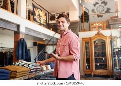 Portrait Of Male Owner Of Fashion Store Using Digital Tablet To Check Stock In Clothing Store