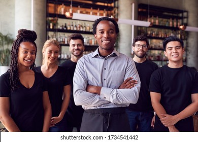 Portrait Of Male Owner Of Restaurant Bar With Team Of Waiting Staff Standing By Counter