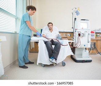 Portrait Of Male Patient Being Prepared By Nurse Before Renal Dialysis In Hospital Room