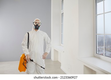 Portrait Of A Male Pest Control Service Exterminator At Work. Young Worker Wearing A Mask And A White Suit Standing Inside The House And Holding His Yellow Spray Bottle With Rodenticide Or Insecticide