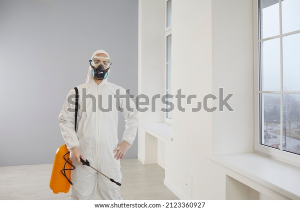 Portrait of a male pest control service\
exterminator at work. Young worker wearing a mask and a white suit\
standing inside the house and holding his yellow spray bottle with\
rodenticide or\
insecticide