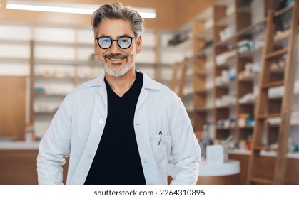 Portrait of a male pharmacist standing in a drug store in a white lab coat. Senior man working in a pharmacy. Mature healthcare worker smiling at the camera. - Powered by Shutterstock