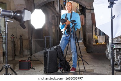 Portrait Of Male Photographer Standing With Camera Among Professional Photo Equipment At Old City Street 