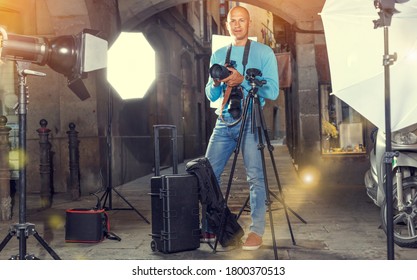 Portrait Of Male Photographer Standing With Camera Among Professional Photo Equipment At Old City Street