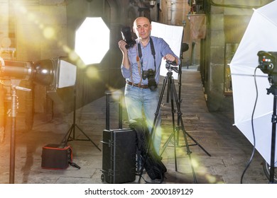 Portrait Of Male Photographer Standing With Camera Among Professional Photo Equipment At An Old City Street