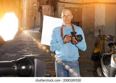 Portrait Of Male Photographer Standing With Camera Among Professional Photo Equipment On Old City Street