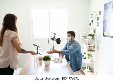 Retrato de un presentador de radio y locutor invitando a su invitado a sentarse para una entrevista mientras ambos usan máscaras durante la pandémica del cóvido 19