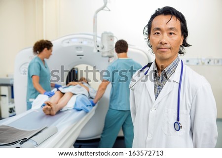 Portrait of male radiologist with nurses preparing patient for CT scan test in hospital