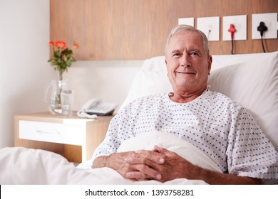 Portrait Of Male Senior Patient Lying In Hospital Bed Smiling At Camera