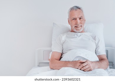 Portrait of male senior patient lying in hospital bed smiling at camera. Old elderly patient grandfather having treatment hospitalized in clinic - Powered by Shutterstock