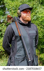 Portrait Of A Male Shooter 30-35 Years Old With A Sports Rifle On His Shoulder, Wearing Glasses And Tactical Headphones For Shooting Against The Background Of Nature.